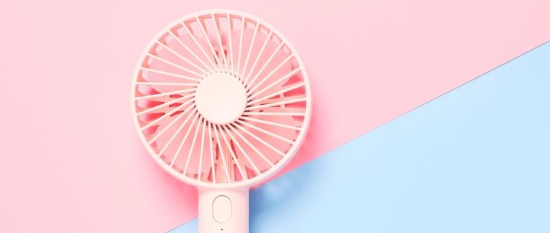 Pale pink free-standing hand-held fan against diagonally split pink and blue background.