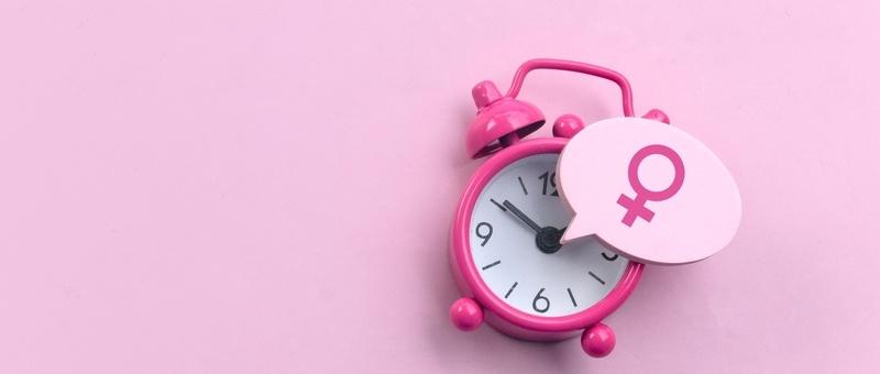 Female gender sign beside pink and white alarm clock against pink background.