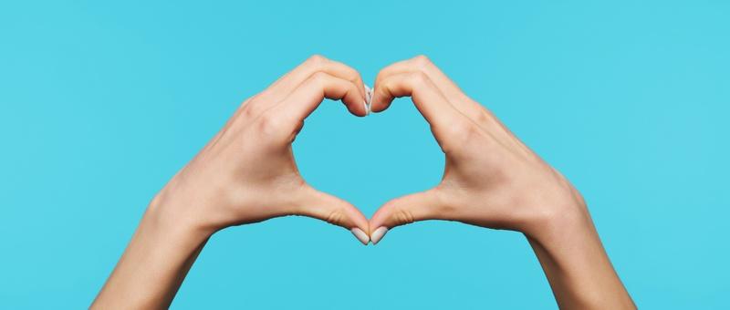Female heart hands against blue background.
