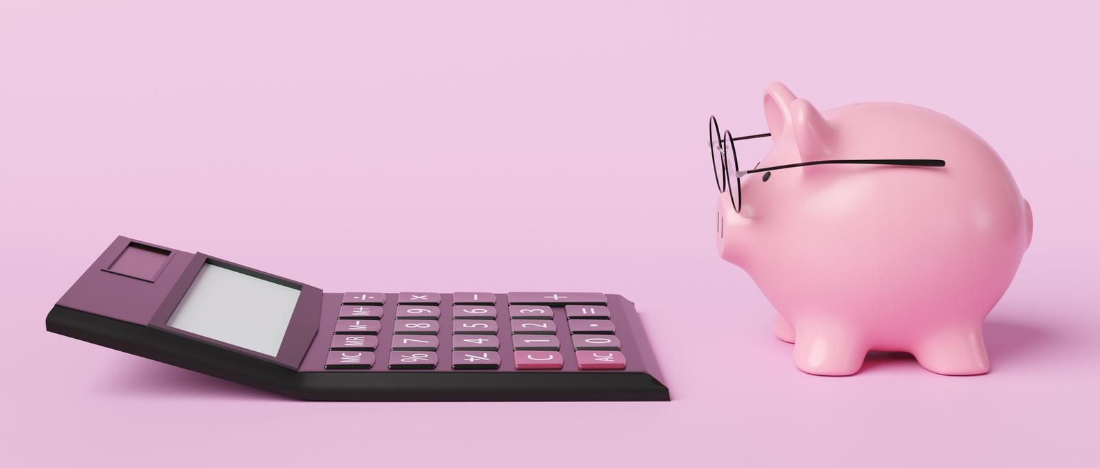 Pink piggy bank wearing spectacles in front of a black calculator on pink background.