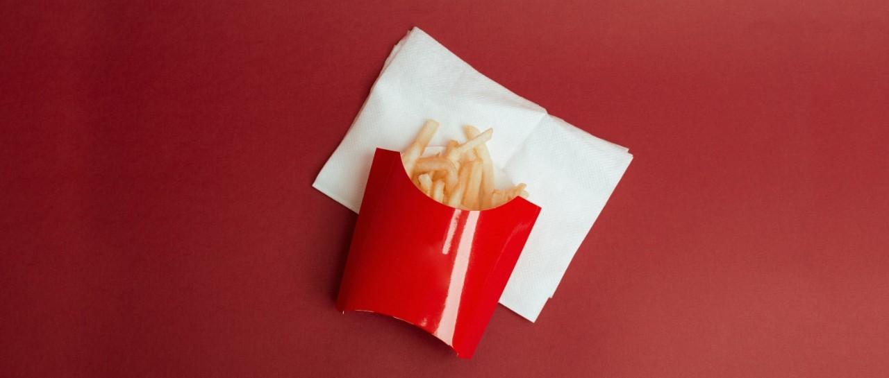 French fries in a red cardboard container on a white napkin against a red background.